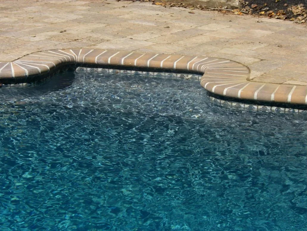 Close view of pool water over medium gray plaster beside brick coping
