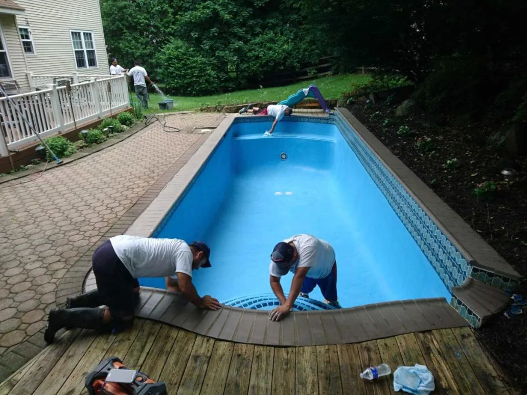 Two Callahan crew members setting coping along a drained pool while a third preps the far wall