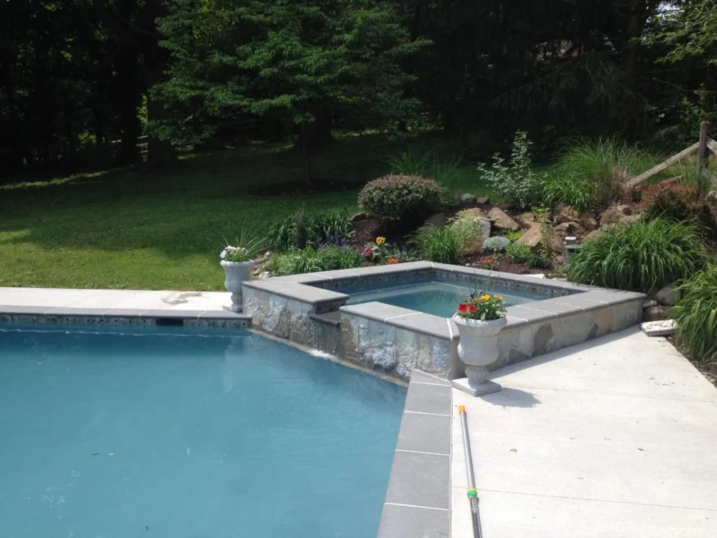 Raised stone-faced spa with gray coping beside the pool